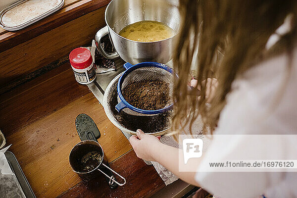 Mädchen siebt Kakao in eine Schüssel  um Brownies herzustellen