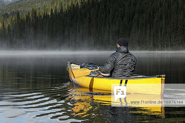 Rückenansicht eines Mannes paddeln Kanu auf ruhigen nebligen See