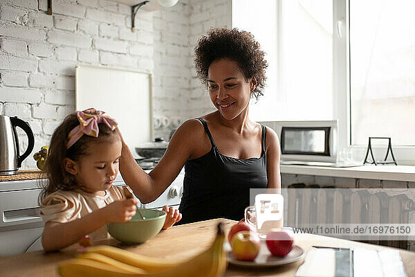 Ethnische Mutter streichelt Tochter beim Frühstück