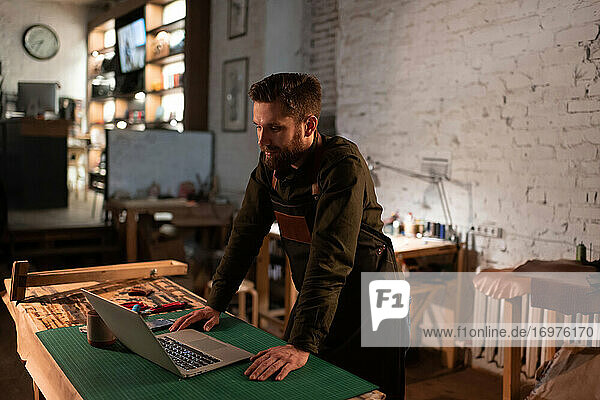 Positiver Kunsthandwerker mit Laptop in der Werkstatt