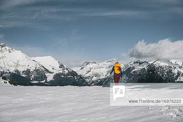 Young man walking in deep snow against snowcapped mountain.