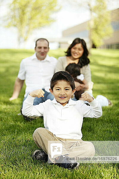 Boy flexing while sitting in front of family in grass