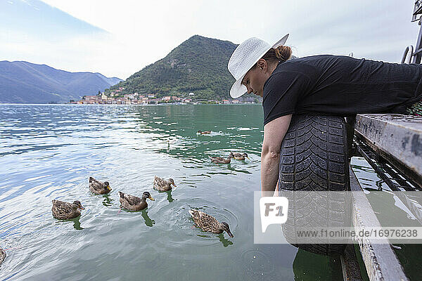 A woman laying down on a dock feeding ducks on a lake in Italy
