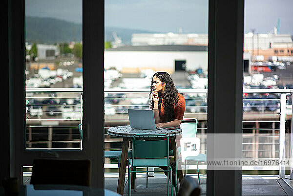 Frau mit Laptop arbeitet am Tisch auf der Terrasse