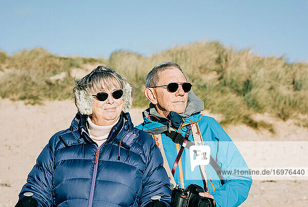 couple in their 70s stood at the beach looking out to the sea