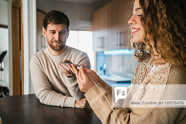 Glückliches Paar  das sein Smartphone in der Küche auflädt