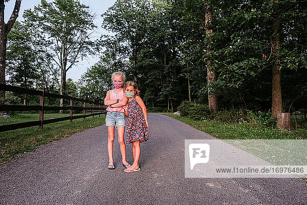 Porträt von zwei Mädchen mit Masken auf der Straße im Wald im Sommer