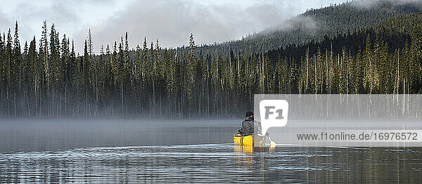 Bärtiger Mann paddelt allein auf einem ruhigen  nebligen See in einem gelben Kanu