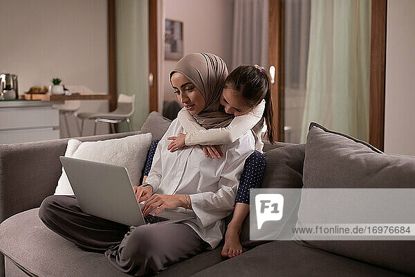 Muslimische Mutter mit Tochter bei der Arbeit auf der Couch