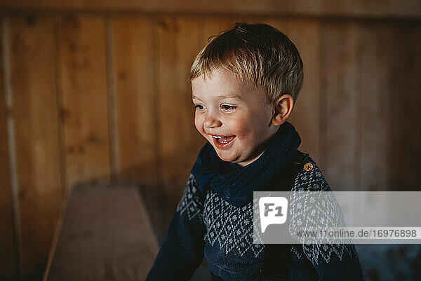 Kleiner Junge trägt lächelnd einen Strickpullover im Winter in einer Holzhütte