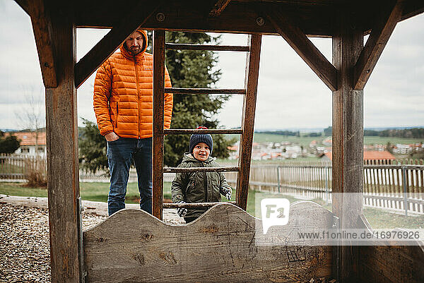 Vater und Sohn auf dem Spielplatz im Winter klettern auf die Leiter zum Holzhaus