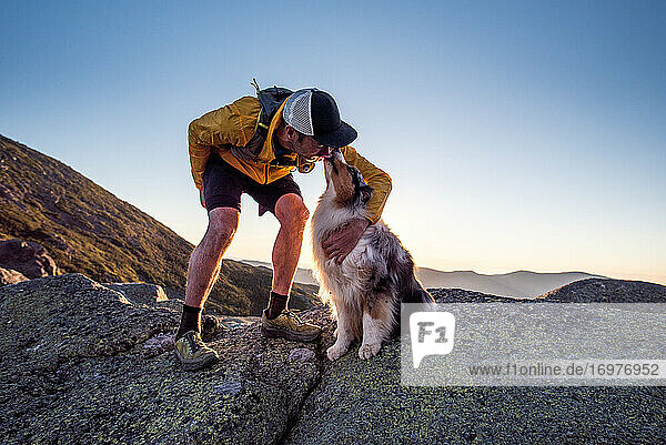 Hund leckt seinem Besitzer das Gesicht beim Trailrunning in den Bergen