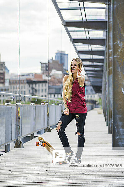Weibliche Skateboarderin mit einem Friedenszeichen und lächelnd downtow