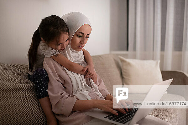 Muslimische Mutter benutzt Laptop in der Nähe ihrer Tochter