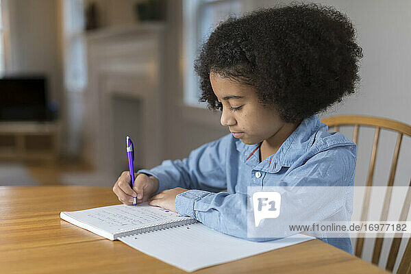 Zehnjähriges gemischtrassiges Mädchen macht am Tisch Hausaufgaben