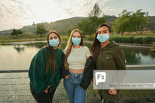 Eine Gruppe schöner junger Freundinnen  die in einem Park posieren und Masken tragen