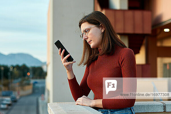 Junge Frau schaut auf einem Universitätscampus auf ihr Smartphone