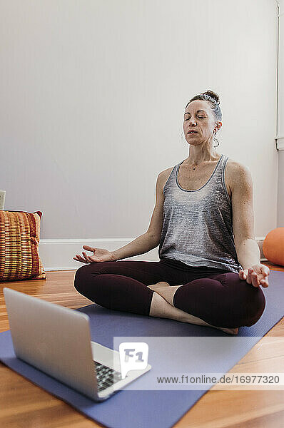 Frau in friedlicher Zen-Position mit Hilfe von Klasse auf Laptop zu Hause