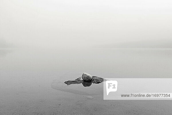 Felsbrocken in noch nebligem See in minimalistischem Schwarz und Weiß