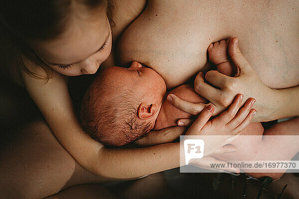 Draufsicht auf ein neugeborenes Baby  das gestillt wird  und eine ältere Schwester  die es umarmt