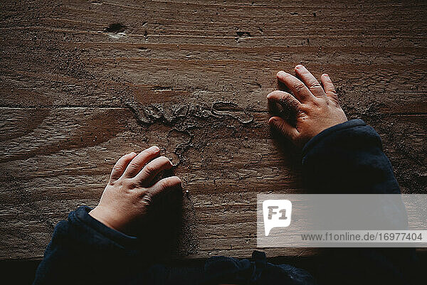 Grübchenhafte Babyhände auf einem Holzbrett voller Sand