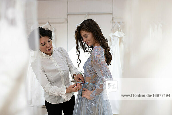 Glückliche Frau bei der Anprobe eines Hochzeitskleides in einem modernen Atelier