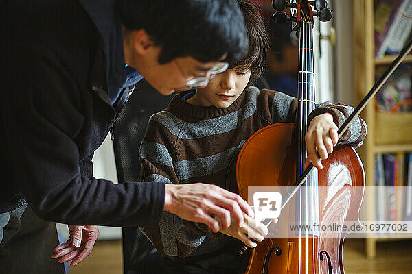 Ein Vater beugt sich vor  um seinem Sohn zu helfen  den Cellobogen richtig zu halten