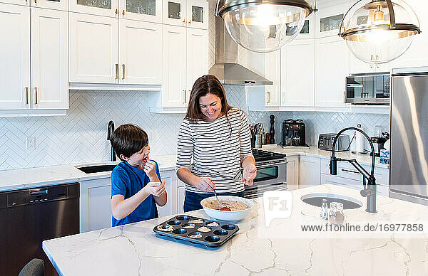 Mother and son making muffins together in a modern white kitchen.