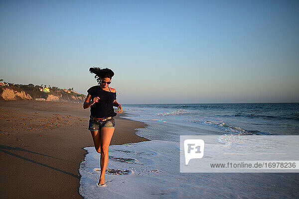 Junge Frau läuft bei Sonnenuntergang am Strand