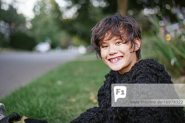 Ein glücklicher Junge im Gorillakostüm lächelt und sitzt auf einer Wiese