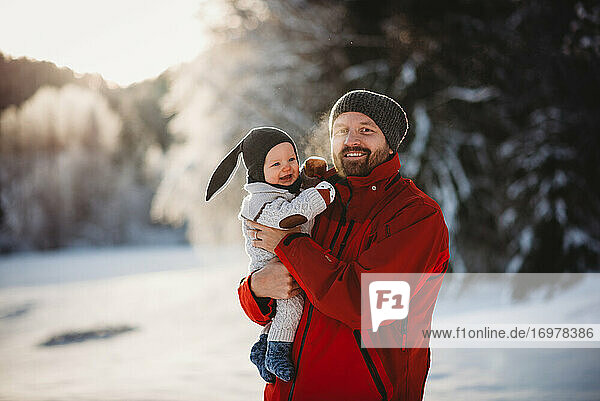 Vater und Baby lächelnd im Winterwunderland voller Schnee im Wald