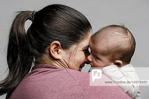 Eine Mutter hält ihr neugeborenes Baby im Arm und betrachtet es liebevoll und lächelnd