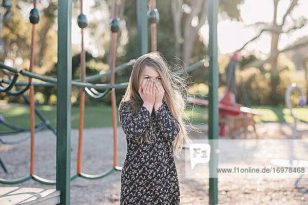Young girl at the playground with her hands on her face