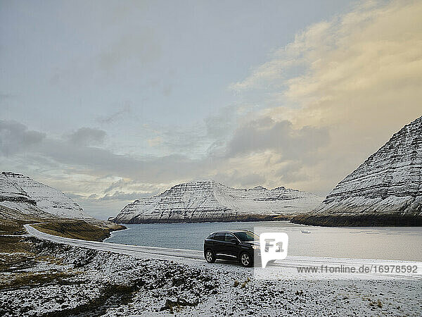 Auto auf verschneiter Straße in Meeresnähe auf den Färöer Inseln