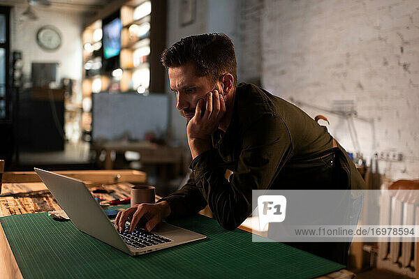 Gelangweilter Handwerker  der im Atelier am Laptop sitzt