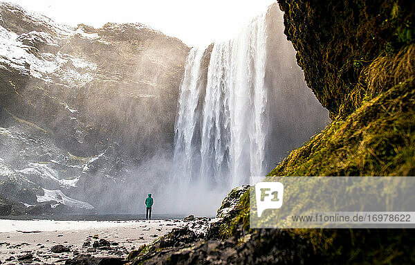 Person am Skogafoss-Wasserfall im Winter mit Moos im Vordergrund
