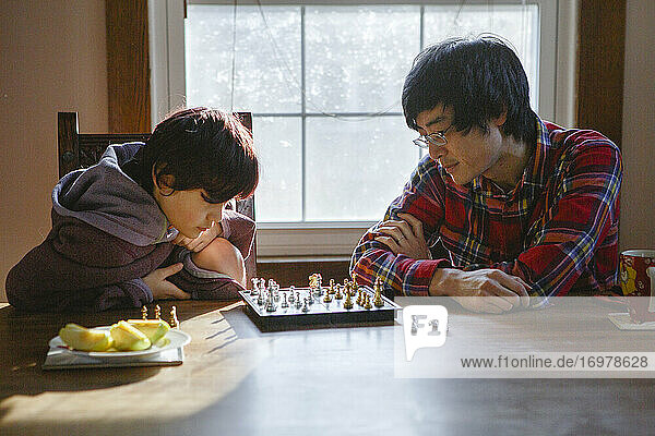 Ein Vater und sein Sohn studieren gemeinsam ein Schachbrett im Fensterlicht