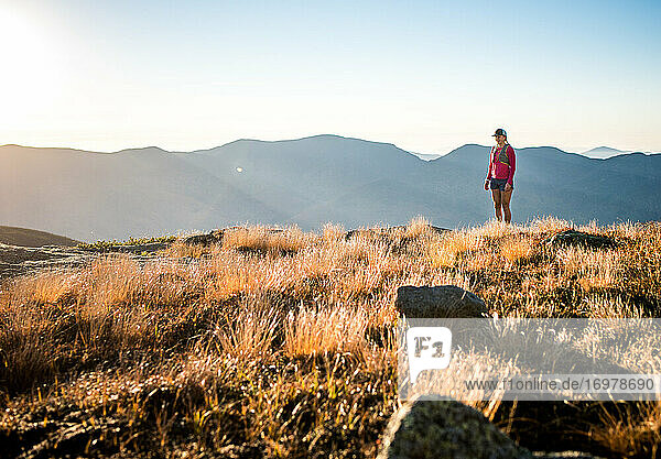 Woman trail-runner standing in the mountains at sunrise