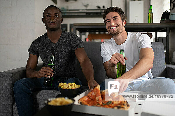 Fröhliche multiethnische Freunde essen Pizza und sehen sich ein Fußballspiel an