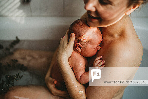 Happy smiling mother holding her newborn baby after being born at home