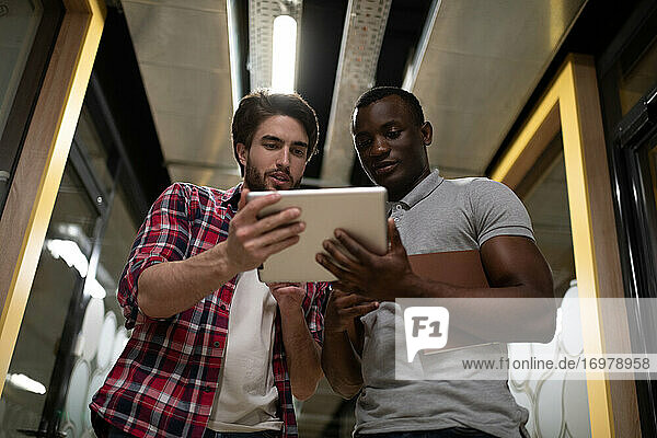 Multiethnic colleagues using tablet in office hallway