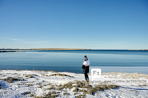 Unerkennbare Frau am verschneiten Meeresufer gegen wolkenlosen blauen Himmel stehend