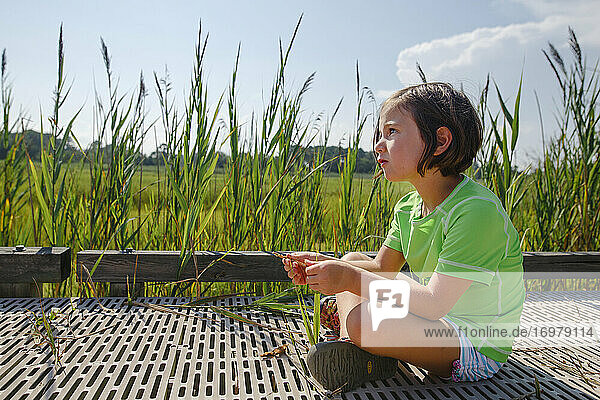 Ein süßes kleines Mädchen sitzt auf der Promenade in einem Feuchtgebiet mit hohem Gras