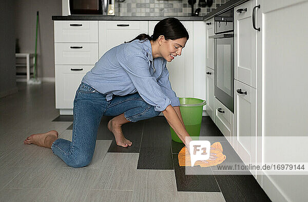 Cheerful woman washing floor in kitchen