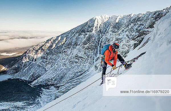 A male climber belays another climber during a winter alpine ice climb