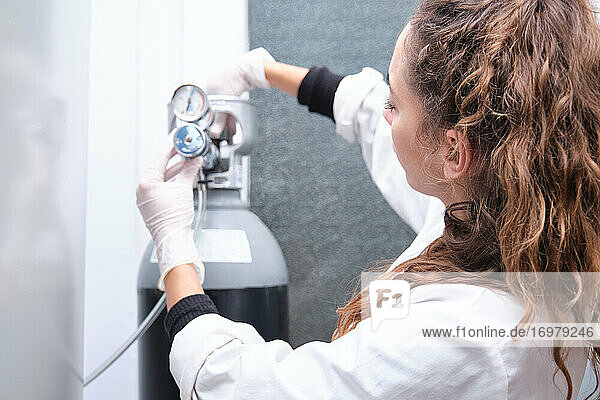 Junge Wissenschaftlerin beim Öffnen einer Gasflasche mit Manometer in einem Speziallabor. Konzept der Laborforschung.