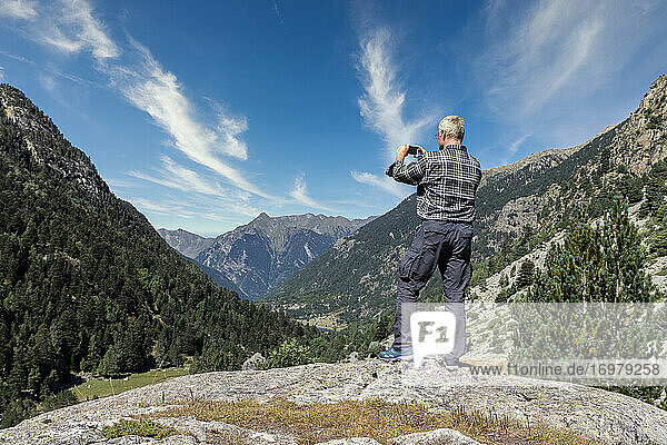 Männlicher Tourist mittleren Alters fotografiert mit seinem Handy in den spanischen Pyrenäen an einem sonnigen Tag