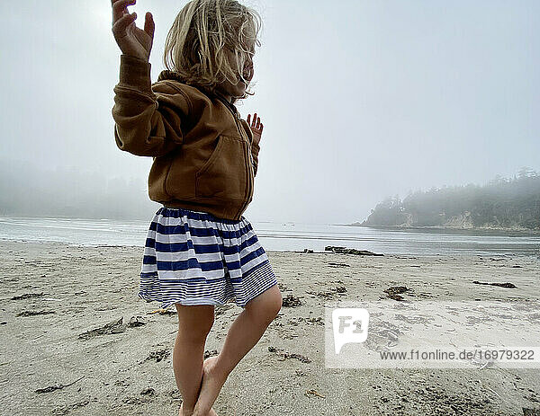 A young girl plays on the beach on the coast of Oregon on a foggy day.