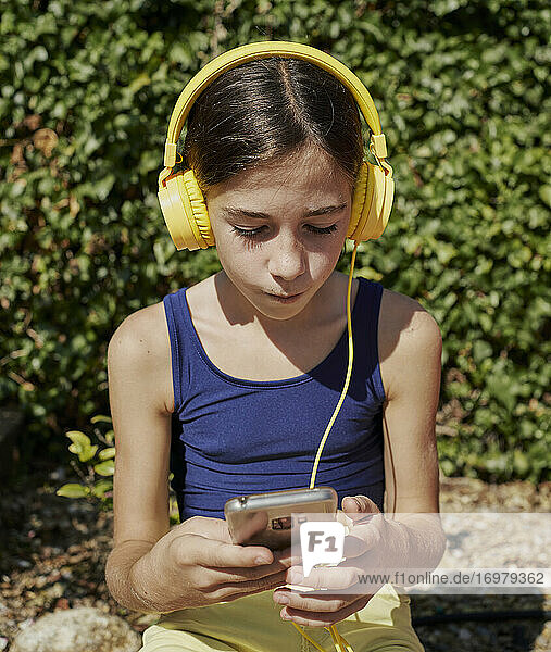 Schönes Mädchen hört Musik mit gelben Kopfhörern und hält ein mobiles Gerät