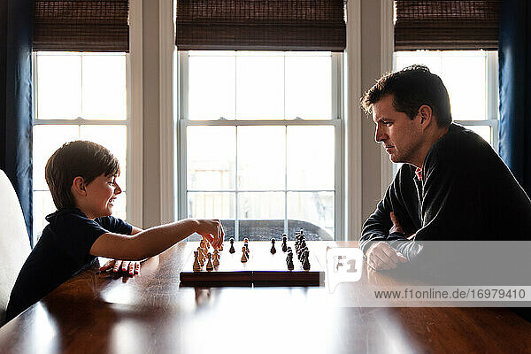 Father and son sitting at a table indoors playing a game of chess.